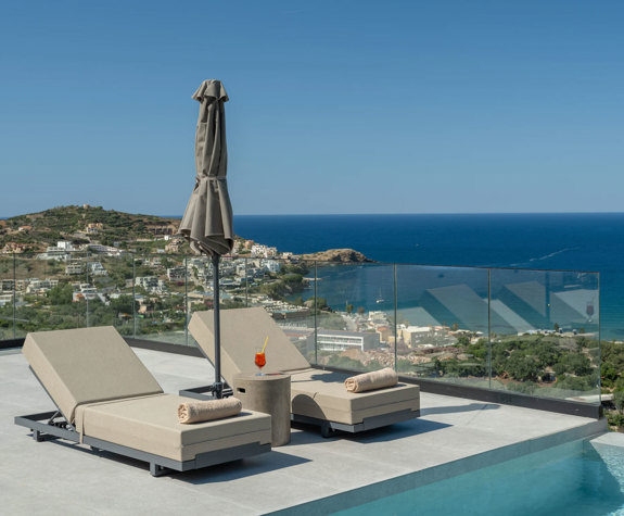Sunbeds on the pool terrace at Nelisa Villa, with a glass balustrade and panoramic sea view.
